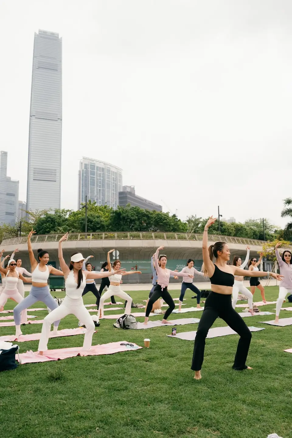 Outdoor barre & yoga class on a lawn with the Hong Kong skyline behind ｜ 戶外草地上的 barre 與瑜伽課堂，背後是香港城市天際線